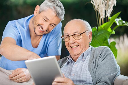 page-produit-netfamille-illustration une jeune homme et une personne âgée rient devant une tablette tactile